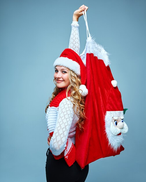Chica vestida con gorro de Papá Noel sosteniendo una bolsa de decoración navideña de Santa Claus en azul