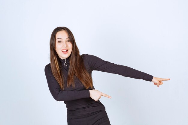 Chica vestida de negro apuntando a algo a la derecha.