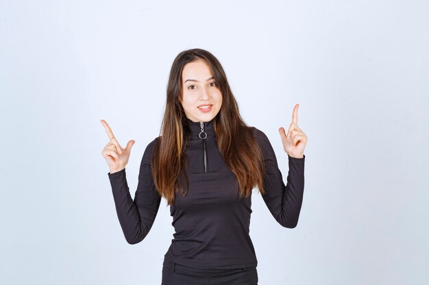 Chica vestida de negro apuntando a algo.