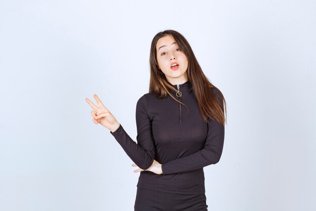 Chica vestida de negro mostrando el signo de la paz y la amistad.