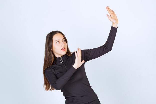 Chica vestida de negro tratando de detener algo.