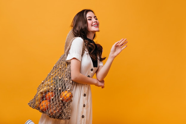 Foto gratuita chica en vestido de algodón con botones marrones posando sobre fondo naranja con bolsa de hilo.