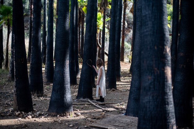 Chica con un vestido blanco en un bosque rodeado de vegetación bajo la luz del sol