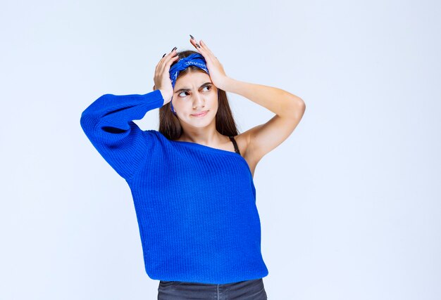 Chica en vestido de fiesta azul sosteniendo la cabeza mientras está confundida y sorprendida.