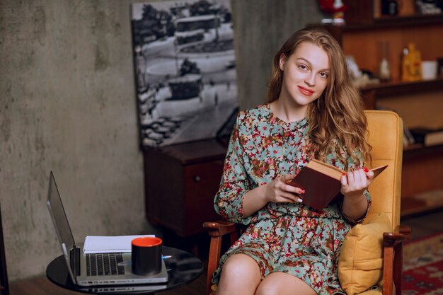 Chica en vestido floral sentado y sosteniendo un libro.