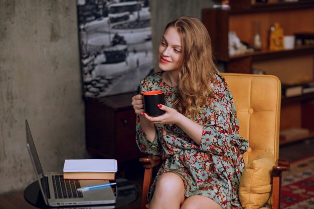 Chica en vestido floral sentado y sosteniendo una taza de café marrón.