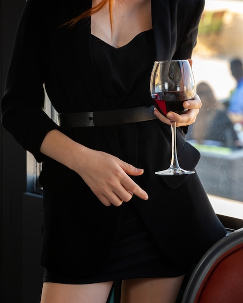 Chica en un vestido negro con una copa de vino tinto