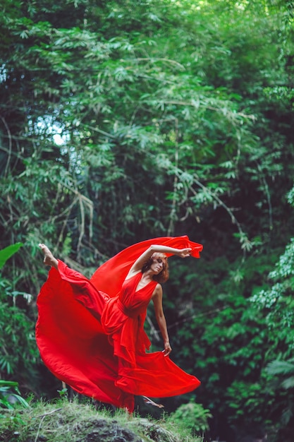 Chica con un vestido rojo bailando en una cascada.