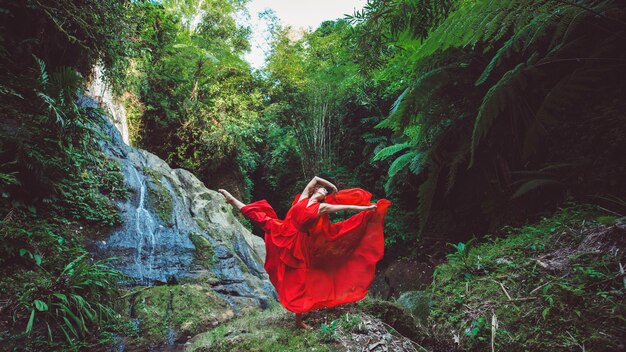 Chica con un vestido rojo bailando en una cascada.