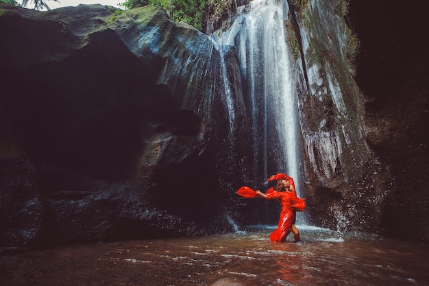 Chica con un vestido rojo bailando en una cascada.