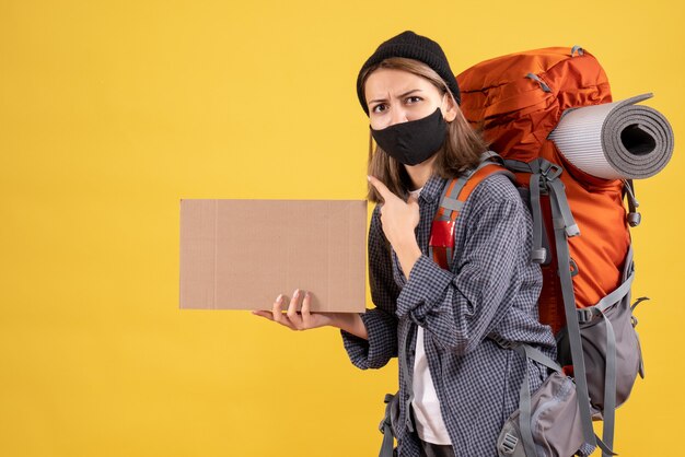 chica viajera con máscara negra y mochila con cartón