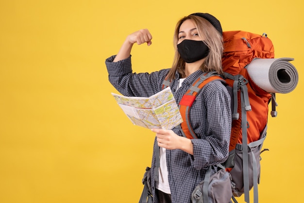 Chica viajera con máscara negra y mochila sosteniendo un mapa que muestra el músculo del brazo