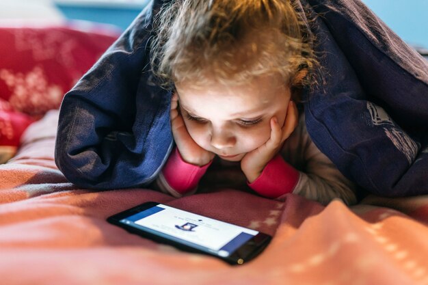 Chica viendo video debajo de una manta