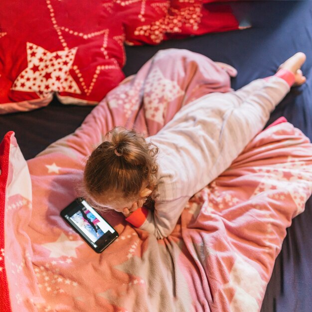 Chica viendo video con el teléfono inteligente en la cama