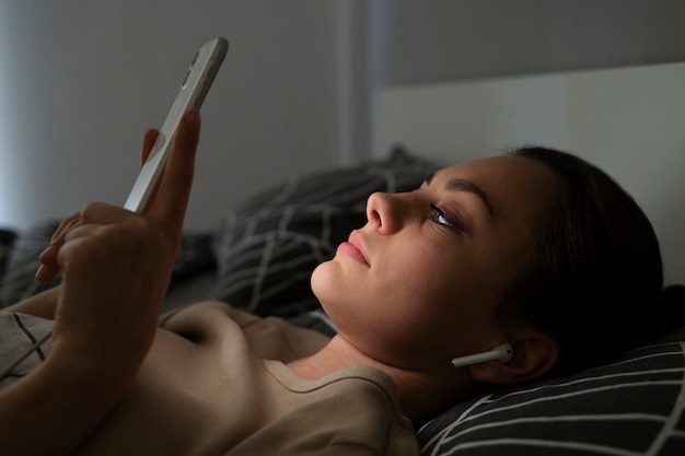 Foto gratuita chica de vista lateral acostada en la cama con teléfono inteligente