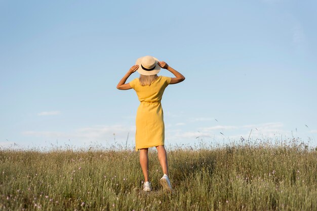 Chica de vista posterior con sombrero dando un paseo en la naturaleza