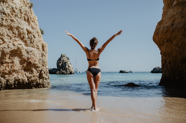 Foto gratuita chica de vista trasera en traje de baño con nalgas sexy se encuentra en piedra grande en la playa durante la puesta de sol.
