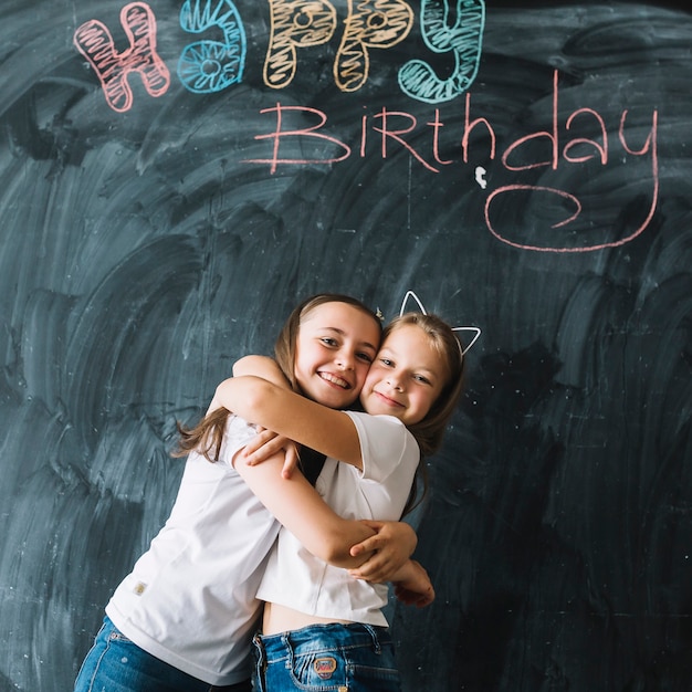 Chicas abrazándose cerca de la escritura del feliz cumpleaños