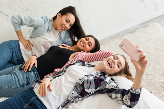 Foto gratuita chicas acostadas en la cama y tomando selfie.