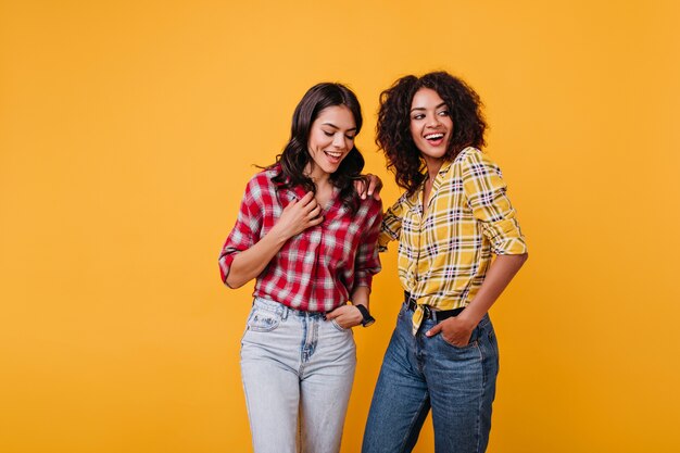 Chicas alegres con elegantes disfraces callejeros se divierten. Morena con brillantes sonrisas posando.