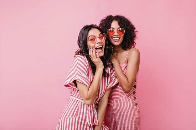 Chicas alegres y extraordinarias con lindos vestidos rosas se divierten. señoras bonitas disfrutando de la sesión de fotos.