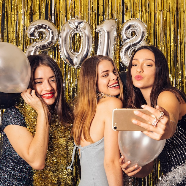 Chicas alegres haciendo un selfie en fiesta de año nuevo