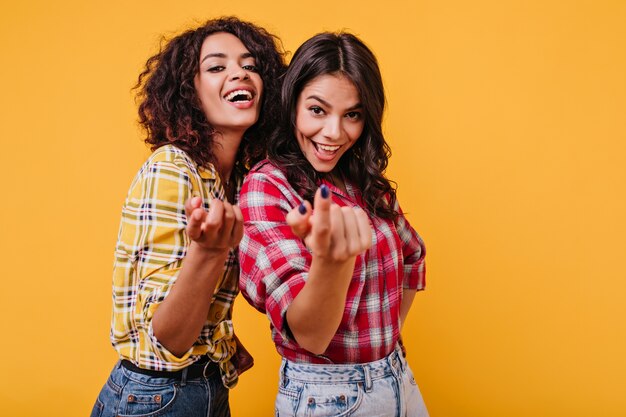 Las chicas alegres sugieren acercarse a ellas. Retrato de alegres morenas sonrientes en traje elegante