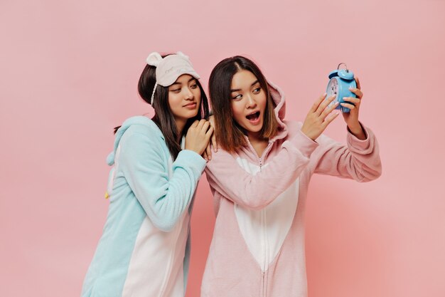 Chicas asiáticas en pijamas lindos coloridos miran el despertador azul