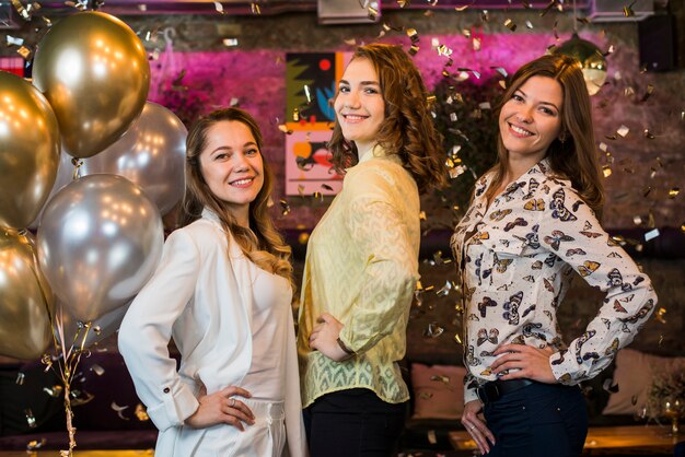 Chicas atractivas posando y sonriendo mientras disfrutan en la fiesta.