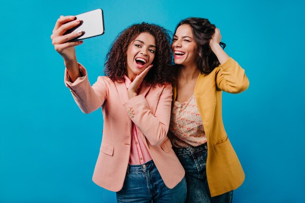 Chicas de cabello oscuro jugando con la foto Foto de estudio de señoritas sonrientes disfrutando de disparar