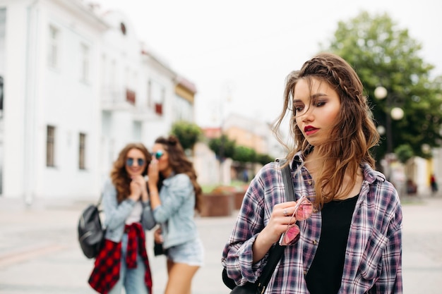 Chicas celosas susurrando sobre la tercera chica frente a la cámara.