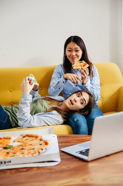 Chicas contentas viendo portátil y comiendo pizza