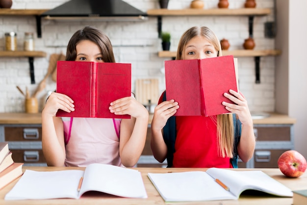 Chicas cubriendo caras con libros.