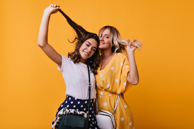 Chicas despreocupadas y bien vestidas jugando con su cabello. damas europeas posando con feliz sonrisa sincera.