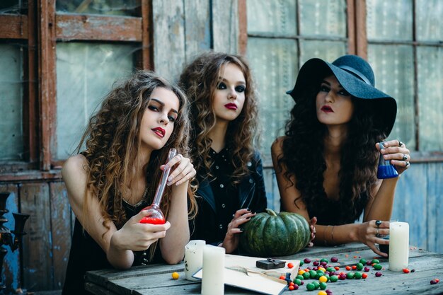 Chicas disfrazadas como brujas sentadas en una mesa con una calabaza y una poción roja y otra azul