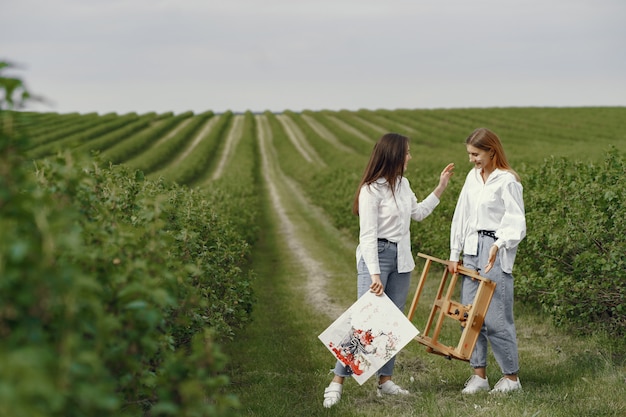 Chicas elegantes y hermosas pintando en un campo