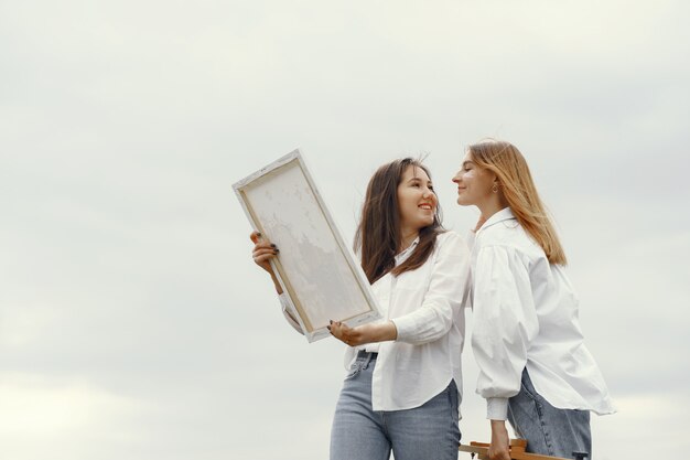 Chicas elegantes y hermosas pintando en un campo