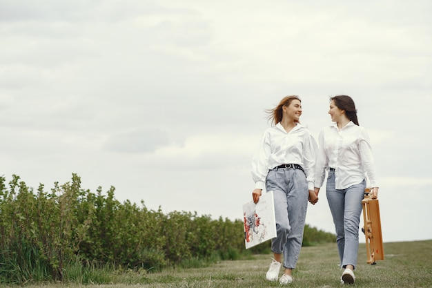 Chicas elegantes y hermosas pintando en un campo