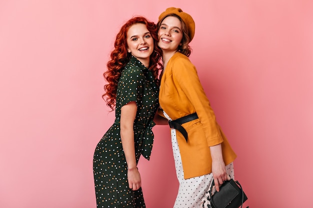 Chicas espectaculares posando juntas sobre fondo rosa. Foto de estudio de hermosas damas mirando a la cámara con una sonrisa.