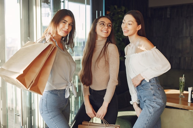 Chicas con estilo de pie en una cafetería con bolsas de compras