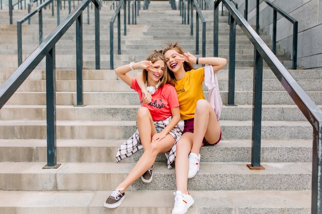 Chicas extasiadas disfrutando de un buen día juntos posando con el signo de la paz y una hermosa sonrisa