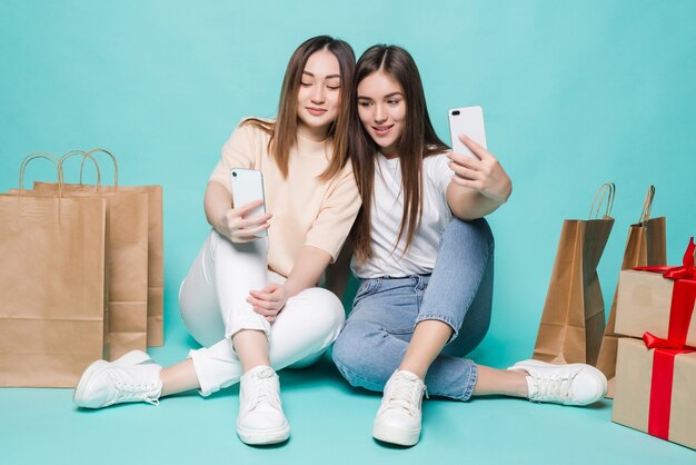 Chicas felices haciendo selfie con bolsas de la compra. Sonriendo a dos niñas en ropa casual colorida tomando fotos