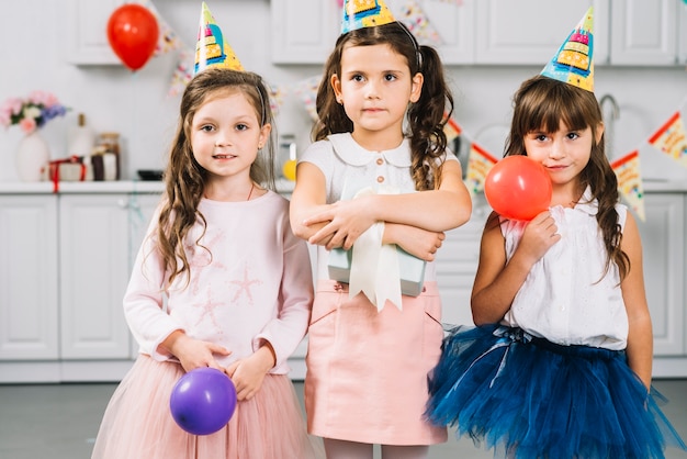 Chicas con globos y regalos de pie en la cocina.