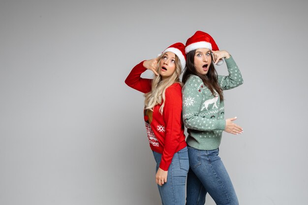 Chicas con gorros de Papá Noel que llaman a través de gestos con las manos.