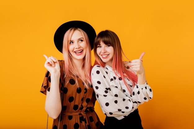 Chicas guapas con cara emocional posando sobre pared amarilla