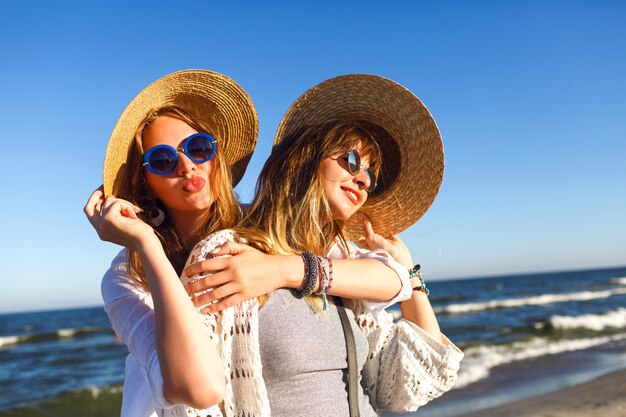 Chicas guapas haciendo selfie y enviando besos al aire a la cámara, viajes de verano, ropa boho, gafas de sol y sombreros de paja