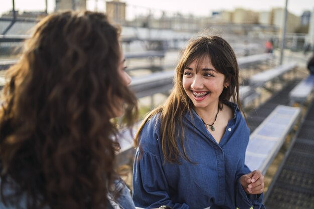 Chicas hablando una al lado de la otra detrás de los edificios.