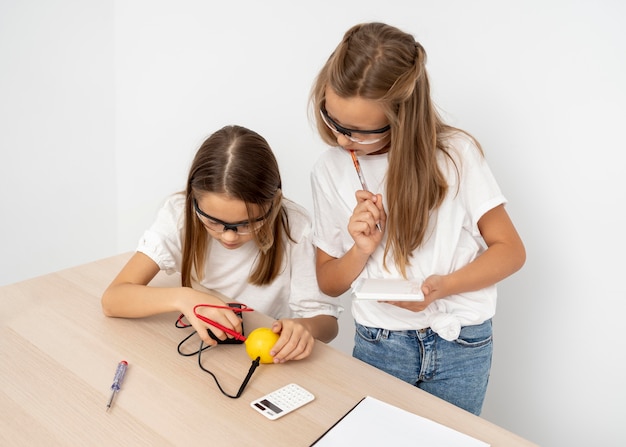 Chicas haciendo experimentos científicos con limón y electricidad.