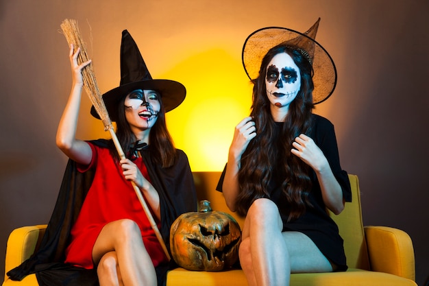 Chicas de halloween en sofá con calabaza y escoba