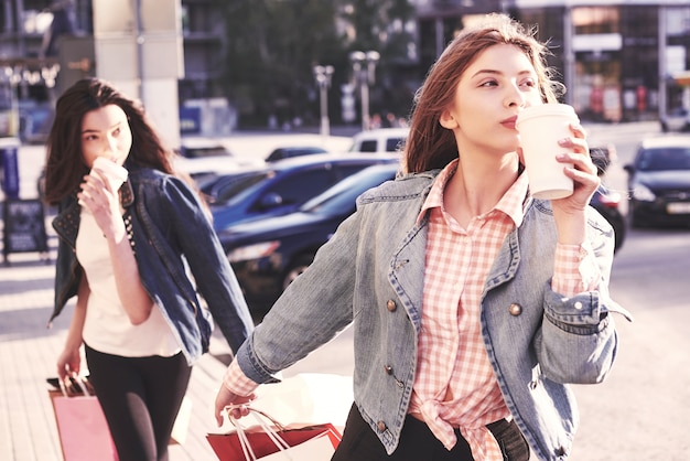 Chicas jóvenes atractivas con bolsas de compras y café en la ciudad.